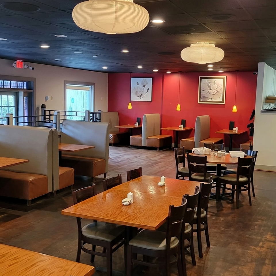 Spacious restaurant dining room with wooden tables, tan booths, red accent wall, pendant lights, and large windows.